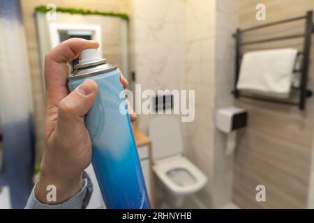 uomo che spruzza deodorante in bagno. deodorante per wc per rimuovere gli odori sgradevoli. ciotola del wc Foto Stock