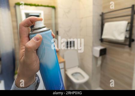 uomo che spruzza deodorante in bagno. deodorante per wc per rimuovere gli odori sgradevoli. ciotola del wc Foto Stock