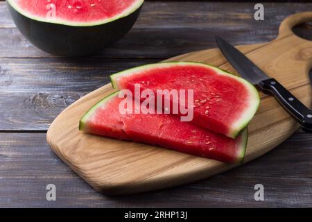 Anguria senza semi, fette su una tavola di legno con un coltello e metà di anguria su fondo di legno. Foto Stock