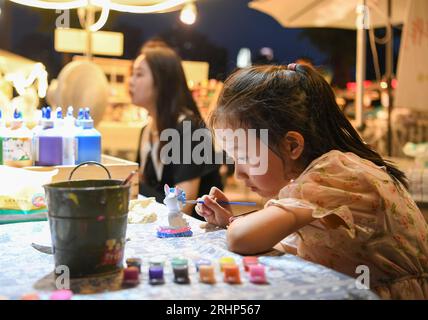 (230818) -- PECHINO, 18 agosto 2023 (Xinhua) -- Un bambino dipinge una bambola in gesso in un mercato notturno nel distretto di Jiangbei, Chongqing della Cina sud-occidentale, 4 agosto 2023. Chongqing, una città sul fiume Yangtze, è chiamata "stufa" dai cinesi a causa della sua alta temperatura estiva; il Cairo, situato sulle rive del Nilo, è stato a lungo un luogo caldo ai margini del deserto. Entrambe le città hanno promosso vigorosamente l'economia notturna. Hongyadong a Chongqing è un'antica porta della città che è stata trasformata in un gigantesco edificio sospeso con ristoranti e altri luoghi di intrattenimento. Kha Foto Stock