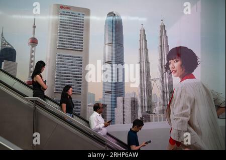 27.07.2023, Singapore, Repubblica di Singapore, Asia - persone su una scala mobile nel quartiere centrale degli affari al Raffles Place di fronte all'annuncio OCBC. Foto Stock