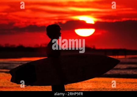 Isola di Palms, Stati Uniti. 18 agosto 2023. Un surfista, sagomato dall'alba, controlla il surf prima di uscire per una mattinata cavalcando le onde in una calda e fangosa giornata estiva nella zona di Charleston, il 18 agosto 2023 a Isle of Palms, South Carolina. Crediti: Richard Ellis/Richard Ellis/Alamy Live News Foto Stock