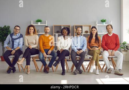 Il pubblico è felice e diversificato, seduto in fila di sedie durante l'evento, nella moderna sala ufficio Foto Stock