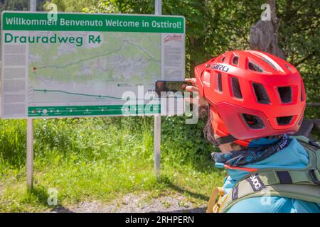 Austria, Tirolo Orientale, ciclista di fronte alla bacheca informativa lungo la pista ciclabile Drau tra San Candido (Innichen) e Lienz Foto Stock