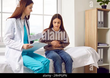 Bambina seduta nello studio del medico che punta al suo stomaco durante l'esame medico in clinica. Foto Stock