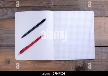 Quaderno scolastico aperto e due penne a sfera su sfondo in legno, vista dall'alto Foto Stock