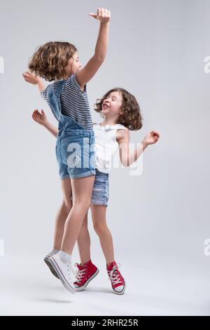 Due ragazze si impegnano in un gioco di salto fisico. Di fronte l'uno all'altro, saltano in alto, si scontrano con le pance e rimbalzano, bilanciandosi con le braccia sollevate. Loro Foto Stock