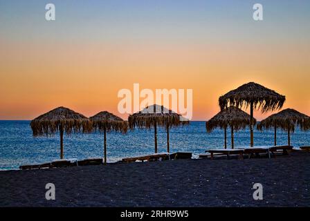 Ombrelloni sulla spiaggia dell'isola di Santorini. Tramonto sulla Grecia. Foto Stock