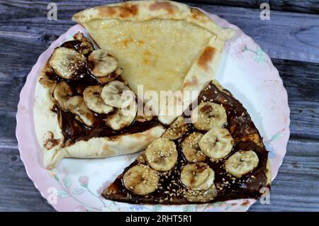 Un piatto di dessert con Una dolce pasticceria di pizza al cioccolato, Chakhtoura, dolce pasticceria al forno, ricoperta di cioccolato, fette di banana, l Foto Stock