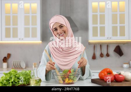 Donna musulmana che prepara una deliziosa insalata con verdure al tavolo bianco in cucina Foto Stock