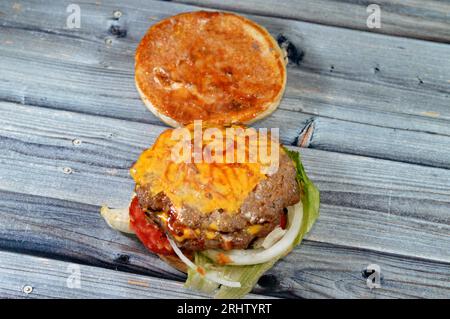 Un succulento e denso polpettine di manzo con formaggio ricoperto di salsa, lattuga croccante, pomodori freschi, cipolle e sottaceti in un panino grande con semi di sesamo, un manzo Foto Stock