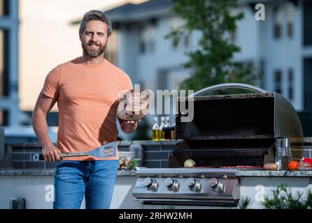 Uomo che si diverte a fare barbecue. uomo che grigia le sue carni preferite. cuoco che mostra le sue tecniche di barbecue durante l'evento di cucina, spazio fotocopie. Irresistibile barbecue Foto Stock