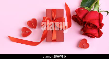 Rose rosse e confezione regalo rossa con fiocco di raso rosso e candele a forma di cuore. Sfondo romantico con spazio per il testo. Buon saluto auto Foto Stock