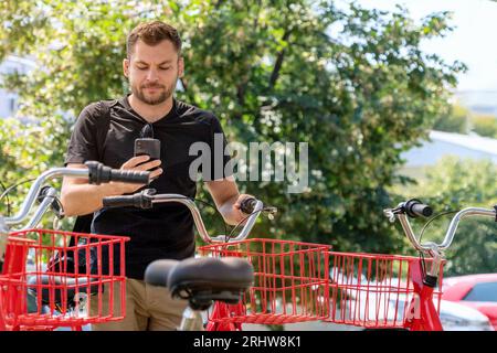 Giovane cittadino che usa il suo cellulare per noleggiare la bicicletta, servizio di condivisione biciclette. Foto Stock