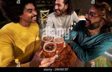 Gruppo di tre amici maschi riuniti in un bar che brindano con le birre, festeggiano insieme e ridono Foto Stock