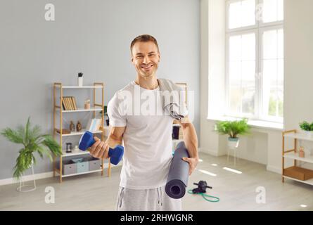 Ritratto di uomo sano e in forma felice con manubri per il fitness e tappetino per l'allenamento a casa Foto Stock