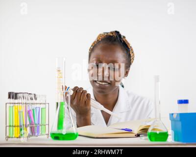 Giovane scienziata che osserva i numeri su una micropipetta in un laboratorio Foto Stock