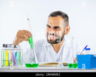 Giovane scienziato maschio che osserva con attenzione un campione di liquido teneva il cilindro di misurazione mentre si trovava in laboratorio Foto Stock