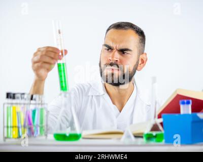 Giovane scienziato maschio che osserva con attenzione un campione di liquido teneva il cilindro di misurazione mentre si trovava in laboratorio Foto Stock