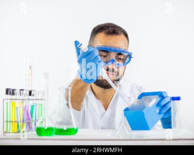 Giovane medico maschio che indossa occhiali protettivi in laboratorio per prelevare un puntale dal portapipette Foto Stock