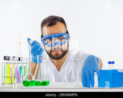 Giovane medico di sesso maschile che indossa glassa protettiva in laboratorio, ponendo un campione in una capsula di Petri con una micropipetta Foto Stock