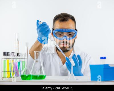 Giovane medico di sesso maschile che indossa glassa protettiva in laboratorio, ponendo un campione in una capsula di Petri con una micropipetta Foto Stock