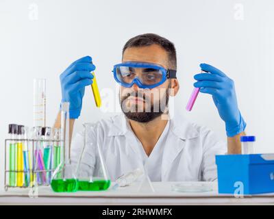 Giovane scienziato maschio che indossa occhiali protettivi confrontando due campioni liquidi in provette Foto Stock