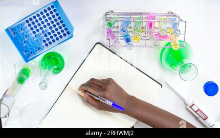 Primo piano di giovani mani femminili che scrivono su un notebook in un laboratorio con attrezzature da laboratorio Foto Stock