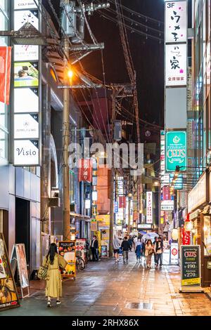 Vista notturna lungo una stradina stretta, Club dori, con ristoranti e ristoranti su entrambi i lati, gente che cammina con ombrelloni sotto la pioggia, Kumamoto. Foto Stock