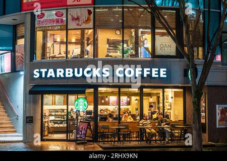 Caffetteria Starbucks di notte sulla via dello shopping Shimotori a Kumamoto. Facciata esterna in vetro con persone sedute all'interno e all'esterno ai tavoli Foto Stock