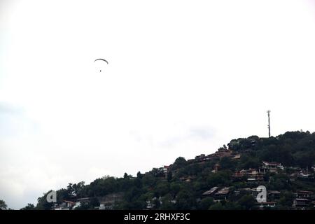 Paesaggio montano con un volo in parapendio in lontananza che vola su un deltaplano attraverso il cielo accanto alla collina Foto Stock