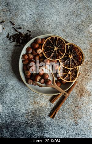 Dall'alto di noci fresche poste in un recipiente di ceramica con bucce d'arancia secche, cannella e chiodi di garofano su fondo di cemento Foto Stock