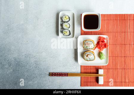 Dall'alto di vari panini di sushi su piatti con bacchette e salsa di soia su sfondo bianco Foto Stock