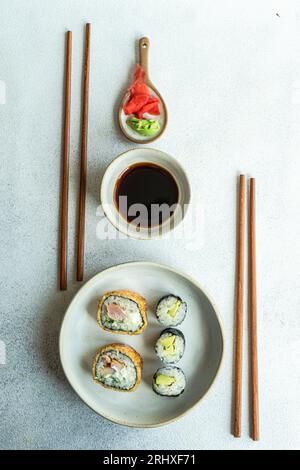 Dall'alto del cibo giapponese con avocado maki roll e sushi fritto con salsa di soia e zenzero su un tavolo di cemento bianco Foto Stock