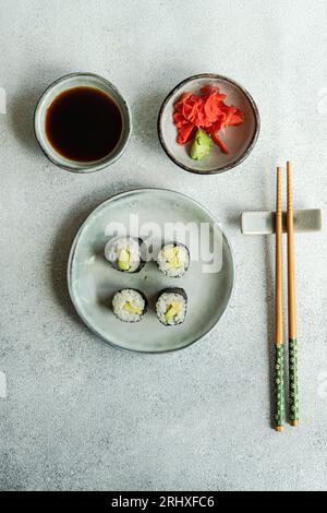 Dall'alto del cibo giapponese con avocado maki roll e sushi fritto con salsa di soia e zenzero su un tavolo di cemento bianco Foto Stock