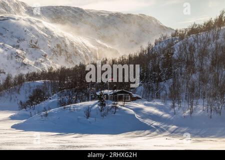 Piccola casa in legno coperta di neve circondata da montagne e alberi in inverno Lapponia Norvegia Foto Stock