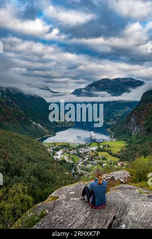 Turista in Norvegia - la donna ammira la vista dal punto panoramico sulla cima di una collina, naviga lungo Geiranger e Geirangerfjorden. Foto Stock