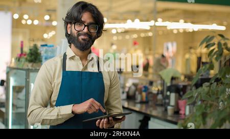 Cameriere maschio indiano in caffetteria che lavora scrivendo ordine cliente in tablet digitale lavoratore caffetteria barista arabo venditore in grembiule annotando il menu giù su Foto Stock