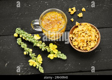 Bevanda a base di tè medicinale a base di erbe fatta di Verbascum thapsus, la grande mulleina, più grande mulleina o comune mulleina. Petali di fiori secchi gialli. Bicchiere di vetro. Foto Stock