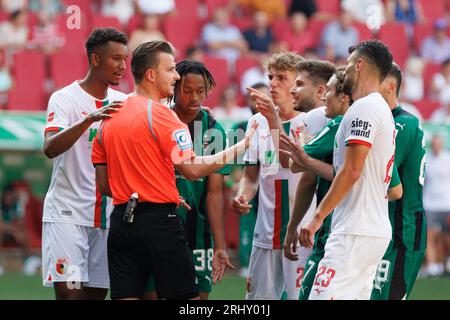 Augusta, Germania. 19 agosto 2023. Calcio: Bundesliga, FC Augsburg - Borussia Mönchengladbach, Matchday 1, WWK Arena. I giocatori di Augusta e Gladbach discutono con l'arbitro Daniel Schlager. Credito: Matthias Balk/dpa - NOTA IMPORTANTE: conformemente ai requisiti della DFL Deutsche Fußball Liga e della DFB Deutscher Fußball-Bund, è vietato utilizzare o far utilizzare fotografie scattate nello stadio e/o della partita sotto forma di immagini di sequenza e/o serie di foto simili a video./dpa/Alamy Live News Foto Stock