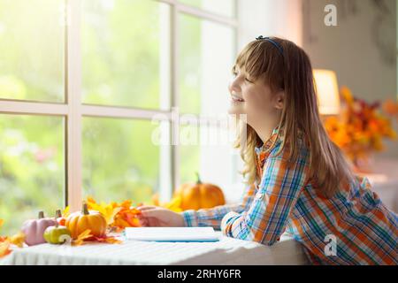 Bambino che guarda fuori dalla finestra. Autunno accogliente casa decorazione. I bambini a casa in autunno guardano le foglie dorate in un giardino soleggiato. Foto Stock