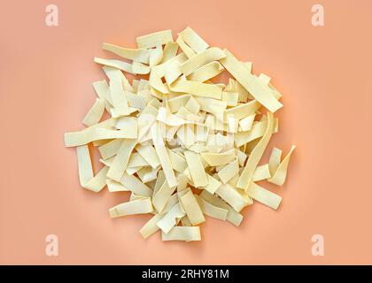 Vista dall'alto degli spaghetti all'uovo. Pasta sottile su sfondo arancione. Spaghetti secchi a righe, pasta. Mucchio di tagliatelle di uova non cotte disidratate gialle Foto Stock