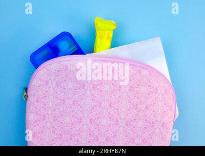 Sacchetto cosmetico rosa con antidolorifici, tamponi e tamponi su sfondo blu. Il concetto di giorni critici, mestruazioni. Set in caso di mestruazioni. Foto Stock