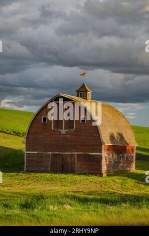 Vecchio fienile rosso (costruito nel 1918) e nuvole serali al tramonto. Contea di Latah, Idaho, USA. Foto Stock