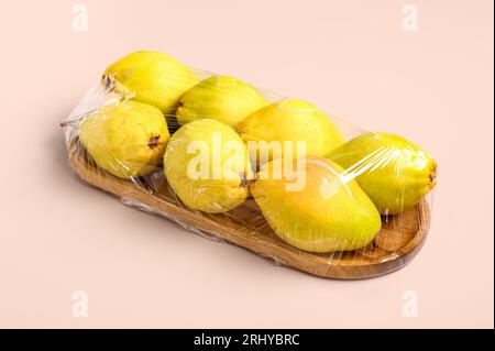Tavola di legno di pere fresche ricoperta da involucro di plastica su sfondo bianco Foto Stock