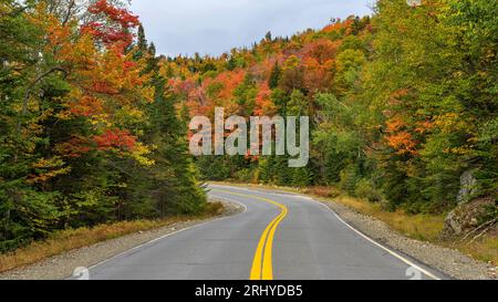 Tortuosa Autumn Road - Highway Route 17, parte della Rangeley Lake Scenic Byway, che si snoda attraverso una colorata foresta di montagna in una mattinata autunnale. Maine, Stati Uniti. Foto Stock