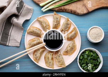 Delizioso gyoza (gnocchi asiatici) con cipolle verdi e salsa di soia servito su un tavolo di legno azzurro, piatto Foto Stock
