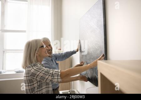 Felice coppia anziana che pende una foto al muro a casa Foto Stock