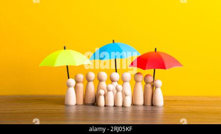 Figure di legno di una famiglia e individui in piedi insieme sotto ombrelli vibranti per la sicurezza Foto Stock