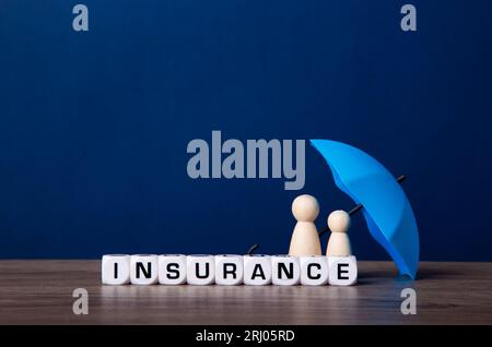 Ombrello giocattolo blu e figure bambola in legno. Concetto di copertura assicurativa. Foto Stock